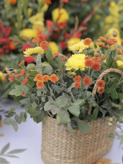 A close-up of the floral arrangements, featuring bright yellow and orange marigolds and chrysanthemums in rustic cane baskets.