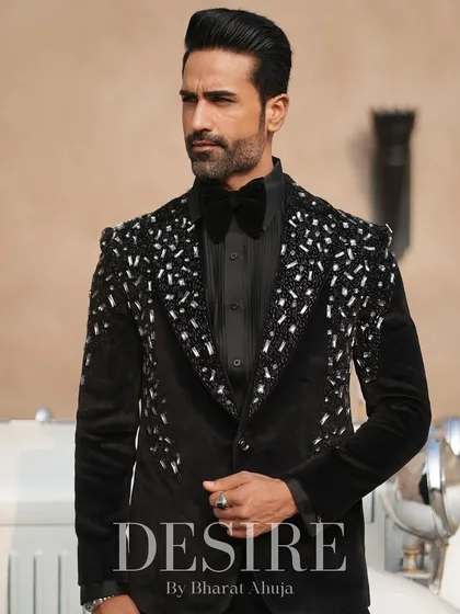 A powerful stance in the black velvet tuxedo with silver scatter embroidery. The vintage car in the background complements the timeless elegance of the suit.