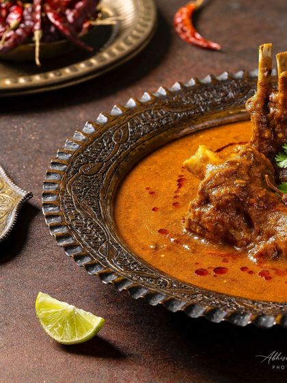 A styled shot of Mutton-e-Rubaruh with dried red chillies and lime, adding color and context.