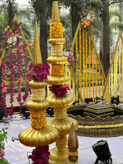 Detailed shot of traditional golden decor pieces adorned with marigold and orchid flowers, set against a modern geometric Haldi backdrop.