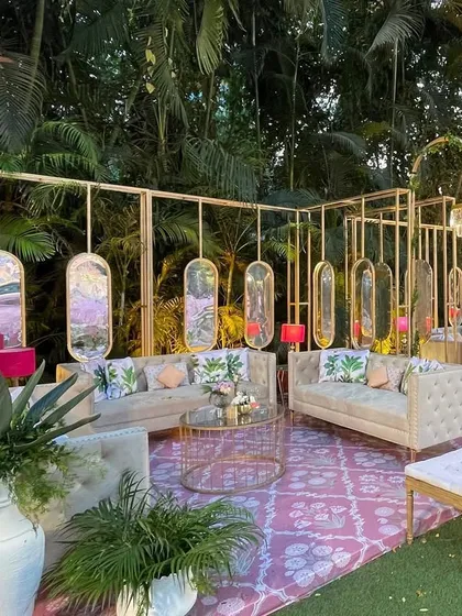 A chic lounge area within the Mamera event, featuring modern gold-framed furniture, tropical print cushions, and hanging mirrors, offering a contemporary twist to the traditional setup.