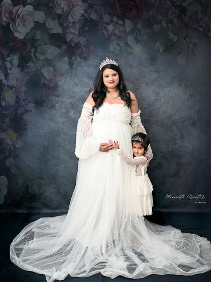 A sweet mother-daughter portrait. The little girl, also in a white dress and tiara, stands close to her mother, creating a precious memory.