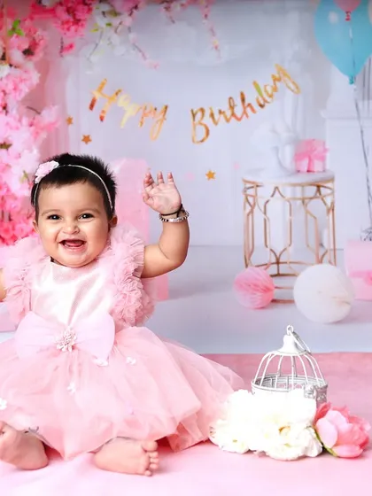 Waving to the camera, this little girl is the star of her first birthday celebration. The pink-on-pink theme creates a soft and dreamy atmosphere.