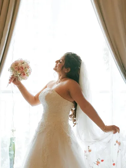 A moment of pure joy. The bride is radiant in the window light, her soft glam makeup enhancing her happy glow.