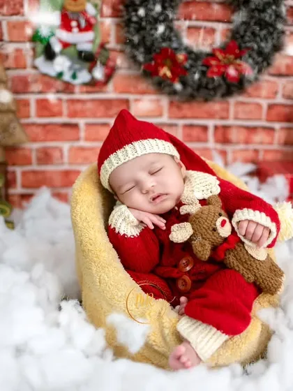 A festive Christmas-themed newborn photo, with the baby dressed in a Santa outfit and sleeping peacefully in a crescent moon prop.