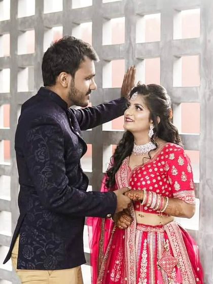 A vibrant and classic wedding look. The bride is glowing in a bright pink lehenga, while the groom looks dashing in a textured navy blue Jodhpuri suit.