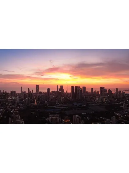 A wide panoramic photograph of the Mumbai skyline at sunset, capturing the city's vastness under a sky filled with warm colors.