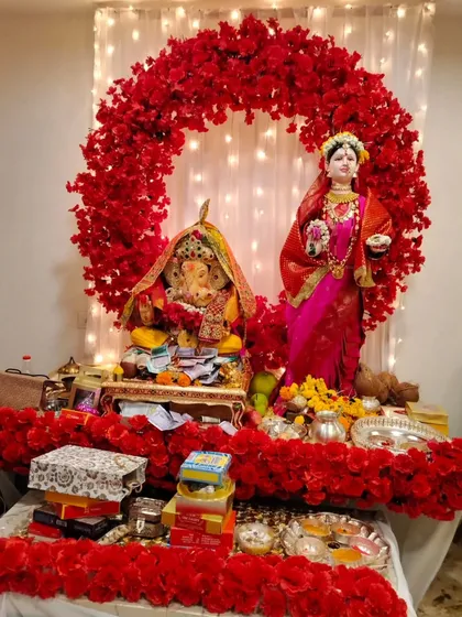 This Gauri Ganpati setup features a bold circular arch of red flowers against a white curtain with fairy lights. The all-red theme creates a striking and powerful festive statement.