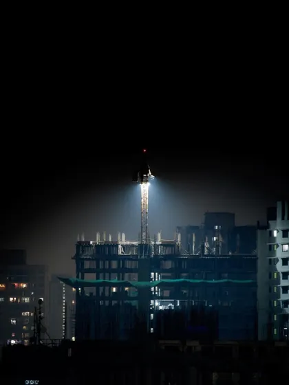 A spotlight on a construction crane at night, creating a solitary, dramatic focal point in the dark city.
