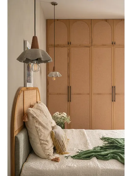 This shot showcases the beautiful concrete pendant lights hanging over the bed. Their unique, fabric-like shape adds an artistic touch, contrasting with the natural texture of the cane headboard and wardrobe.