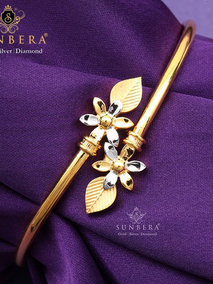 This gold bracelet showcases two delicate flowers with two-tone petals, creating a beautiful contrast. It's a feminine and elegant piece perfect for gifting or personal wear.