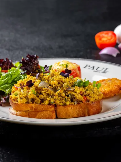 Akuri on toast, a classic Parsi scrambled egg dish, photographed for PAUL India. The dark, slate background makes the colors of the dish and salad pop.