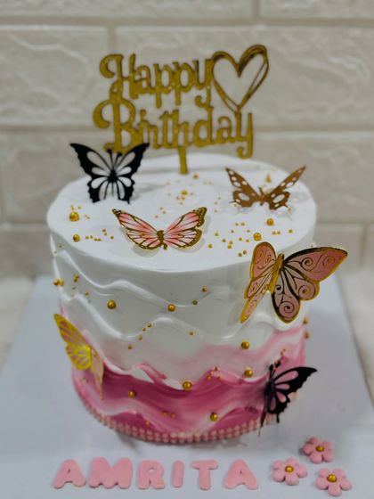 A delicate butterfly cake with a pink ombre wave design. The wafer paper butterflies in shades of pink, gold, and black seem to float around the cake.