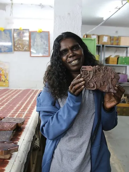 An artist from the Bábbarra Women's Centre proudly holds a woodblock carved from her design. This project is about translating ancestral stories from one medium (lino) to another (wood).