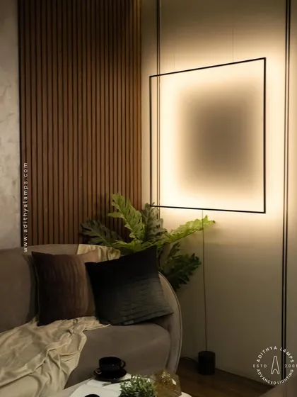 We designed this suspended black frame fixture to be a piece of art in itself. It hangs from the ceiling and is grounded to the floor, creating a striking geometric statement. The light washes the wall with a soft, ambient glow, adding depth and character to this contemporary living space next to the wood-paneled wall.
