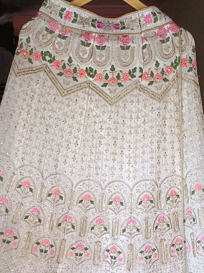 A detailed shot of a beautiful white lehenga with pink and green floral embroidery, a fresh look for a summer wedding.
