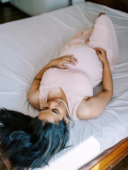 A peaceful moment of rest for the mother-to-be. Lying on the bed in a soft pink dress, this overhead shot captures a feeling of calm and serenity during the final stages of pregnancy.