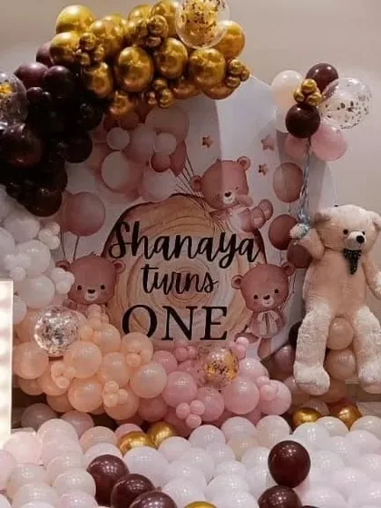 A teddy bear themed first birthday party with a "cloud" of balloons. This decoration features a wooden-textured backdrop, a marquee number '1', and a large teddy bear.