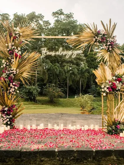 A daytime view of the proposal stage, set against a serene lake. The boho arch with golden palms and deep florals stands out beautifully.