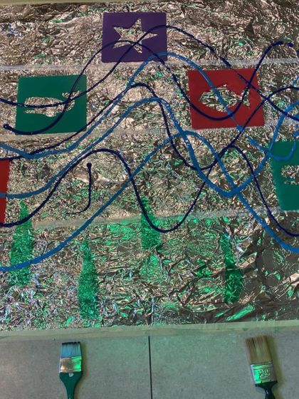 A simple setup for exploring art and reflection. Foil on the floor with stencils and paint invites children to see how light and color interact on a shiny surface, creating a dynamic and engaging art experience.