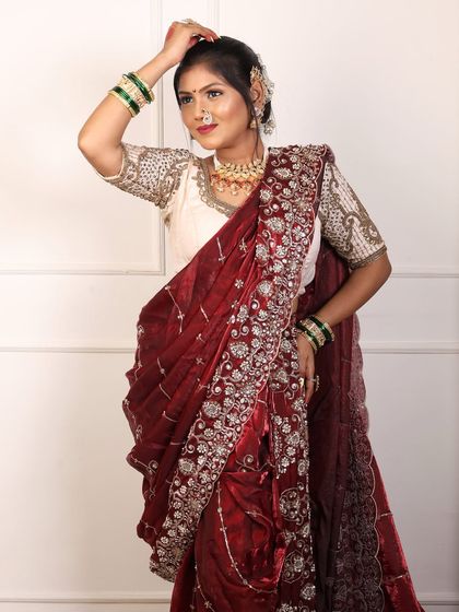 A graceful pose highlighting the flow of the maroon saree and the detailed work on the blouse.