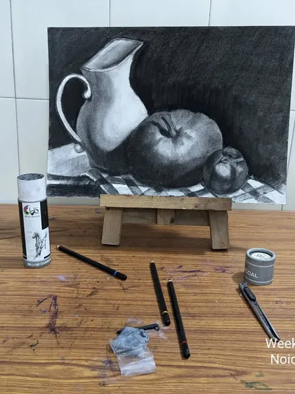 The artist's setup for charcoal drawing. The finished artwork is displayed on a mini easel, surrounded by the tools used to create it.