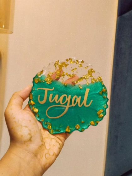 A personalized resin name plaque for 'Jugal'. This geode style coaster features a rich green color, gold flakes, and custom calligraphy, making it a great desk accessory or gift.