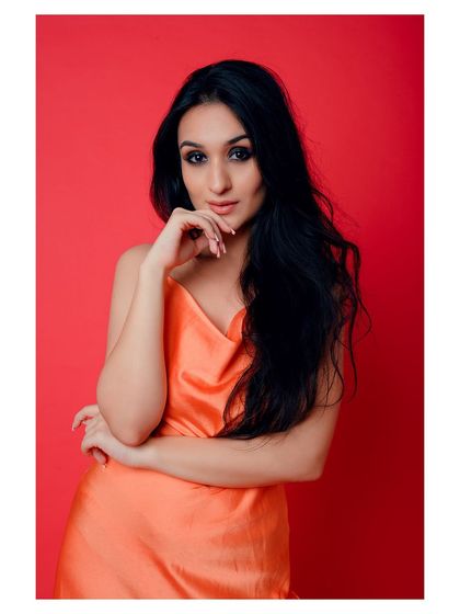 A close-up portrait with a bold red background. The model's direct gaze and the vibrant color create an intense and captivating image.