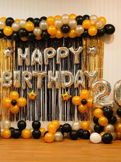 A classic black and gold theme for a 20th birthday. This setup includes a gold tinsel backdrop, 'Happy Birthday' foil letters, and a balloon garland with matching '20' number balloons.