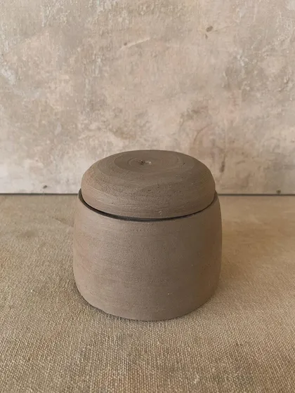 A simple, unglazed lidded jar. The beauty is in its raw, elemental nature and the visible marks of the maker's hands.