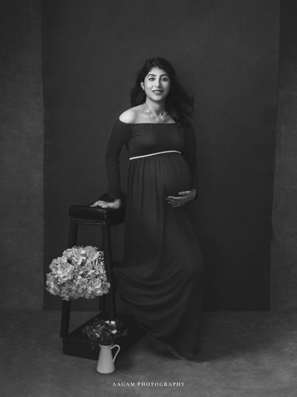 A classic fine art portrait in black and white. The monochrome tones enhance the textures of the gown and the soft expression of the mother-to-be.