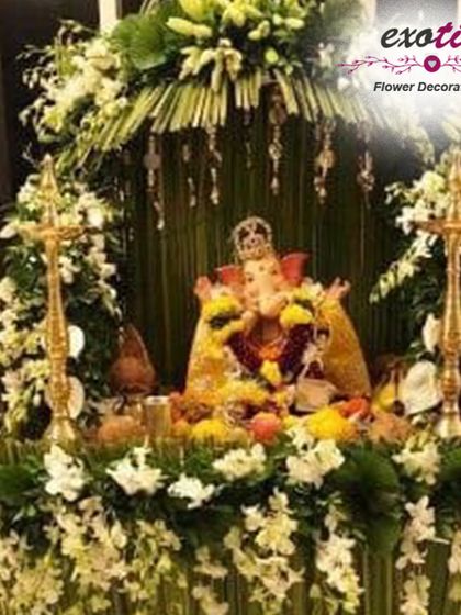 An elegant Ganpati mandap made with white orchids and woven palm leaves, flanked by traditional brass lamps (samai). This design combines natural textures with the purity of white flowers for a sophisticated and serene look.