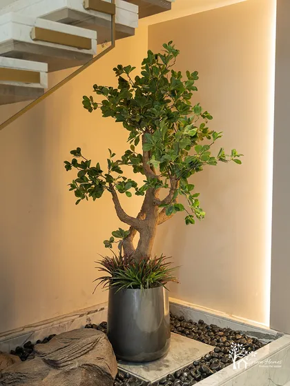 A full view of the under-staircase garden, showing the interplay of the faux tree, rocks, pebbles, and vertical accent lighting. The result is a complete and polished look.
