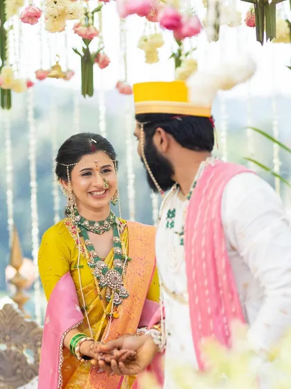 A close-up of the couple sharing a glance during their wedding ceremony. This shot highlights the bride's exquisite emerald green jewelry, which beautifully contrasts with her yellow and pink saree.