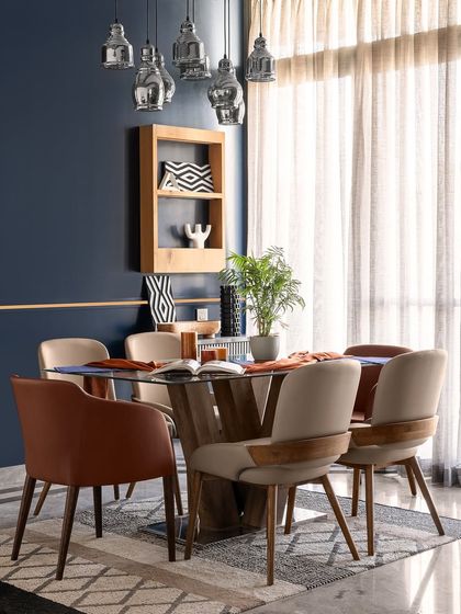 The dining space in Apartment 704, where a glass-top table with rustic wooden legs is surrounded by chairs in two different leatherette colors. This balances the vibrancy of the blue accent wall and hanging lights.