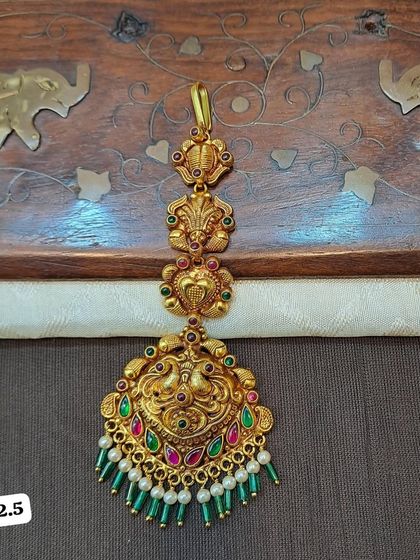This 92.5 silver gold-plated maang tikka features an intricate peacock design. It is embellished with red and green stones and a mix of green beads and pearls.