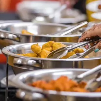 A guest selecting fresh pakoras from a chafing dish at an event. We ensure all our food, especially fried items, is served hot and fresh for the best taste and texture.