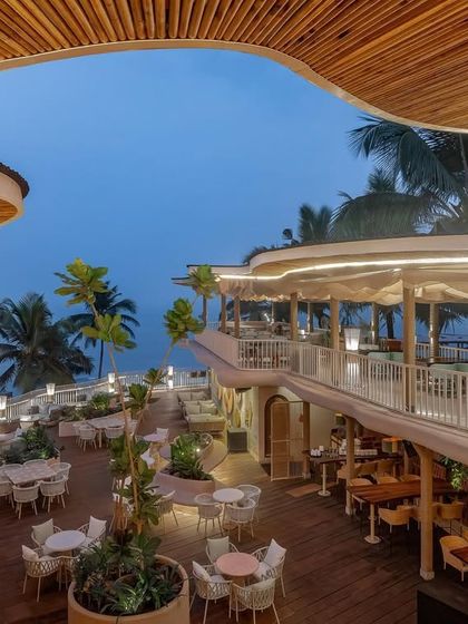 As dusk settles over Dubki in Goa, the architectural lighting highlights the unique, wave-like roof structure and the multi-level layout. The space transforms into an intimate, atmospheric setting against the backdrop of the evening sky.