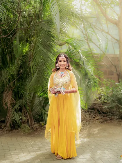 A full-length shot of the bride in her yellow Haldi outfit, adorned with our custom pastel floral jewellery set.