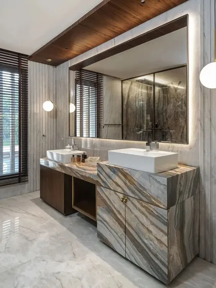 A double vanity crafted from two different types of marble, creating a dramatic, high-contrast look. The large backlit mirror and globe pendant lights add a layer of sophisticated lighting.