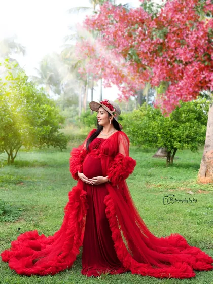 A dreamy outdoor portrait in a red ruffled gown and hat. The soft lighting and beautiful garden create a magical atmosphere.