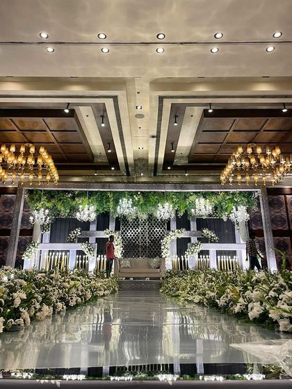 A luxury reception stage with a mirrored floor, reflecting the lush greenery and elegant chandeliers. This design creates a sense of grandeur and opulence.