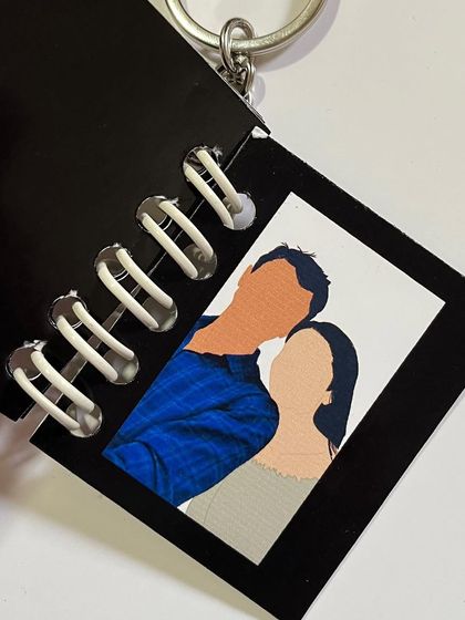 A close-up of an open booklet keychain, showing the faceless illustration inside.