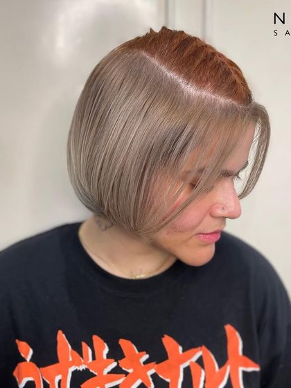 A creative peekaboo hair color. This look features a cool blonde bob with a hidden pop of coppery red underneath, offering a fun and surprising twist.