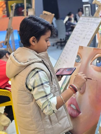 A young student works on a large portrait, using his phone for reference. We encourage ambition and provide the tools for students to tackle challenging projects.