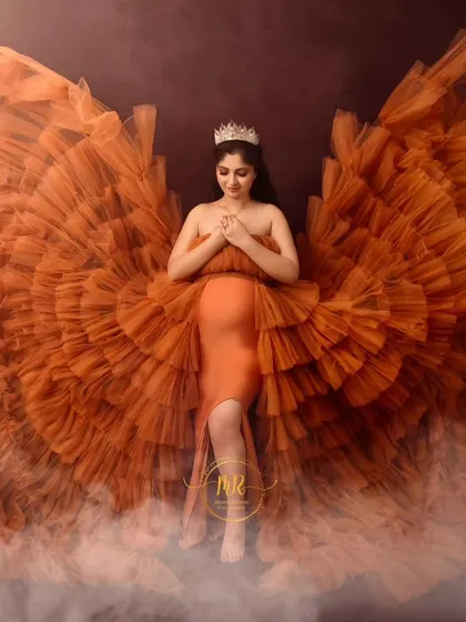 An angelic fine art portrait. The mother-to-be wears a crown and a magnificent orange gown styled into wings, surrounded by a soft mist for a heavenly look.