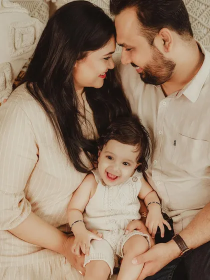 A joyful family portrait, with parents looking lovingly at each other while their baby smiles at the camera. A perfect capture of family happiness.