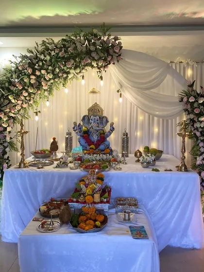 A beautiful home Ganpati setup featuring an asymmetrical arch of pink and white roses, with soft lighting to create a warm glow.