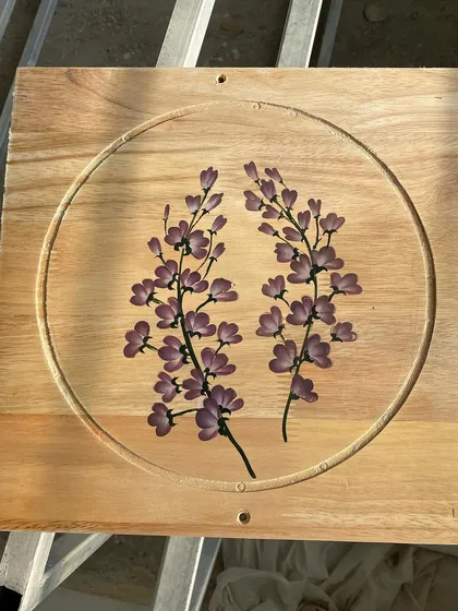 Sprays of lavender-colored flowers on a square wooden panel. The circular groove frames the artwork beautifully.