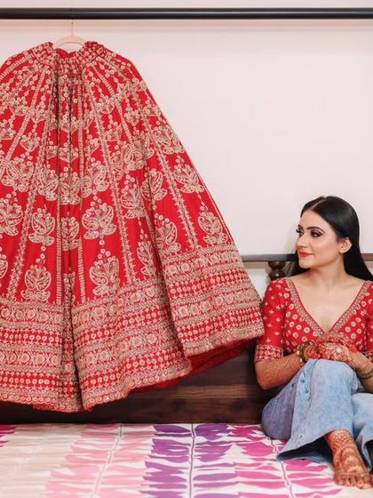 A pre-getting ready shot. The bride, with her base makeup on, sits with her magnificent red lehenga.